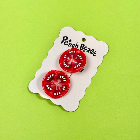 Red tomato-shaped earrings on a 'Peach Beast' branded card against a green background