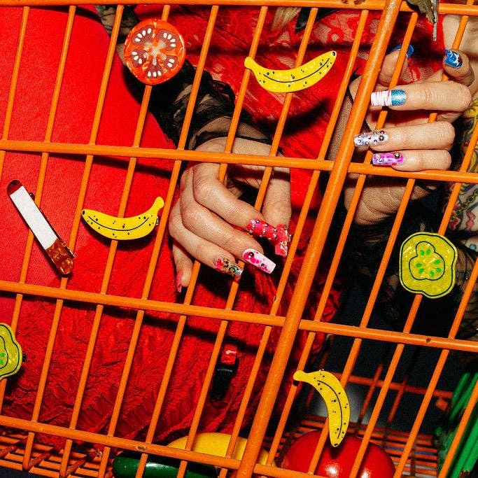 Person with colorful nail art behind an orange cage with decorative hair clips.