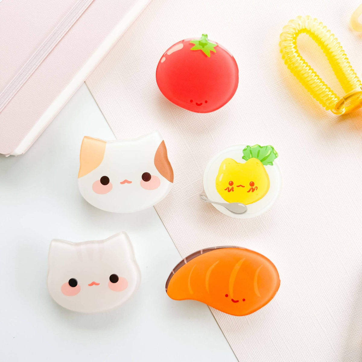 Set of cute, cartoon-style erasers shaped like a cat, tomato, pineapple, and sushi on a white surface.