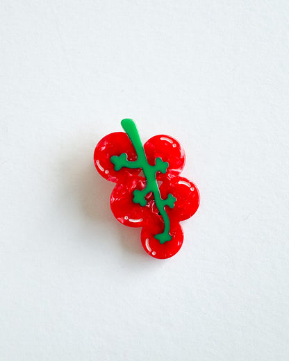 A small glossy red berry cluster accessory with a green stem and leaves, photographed on a plain white background.