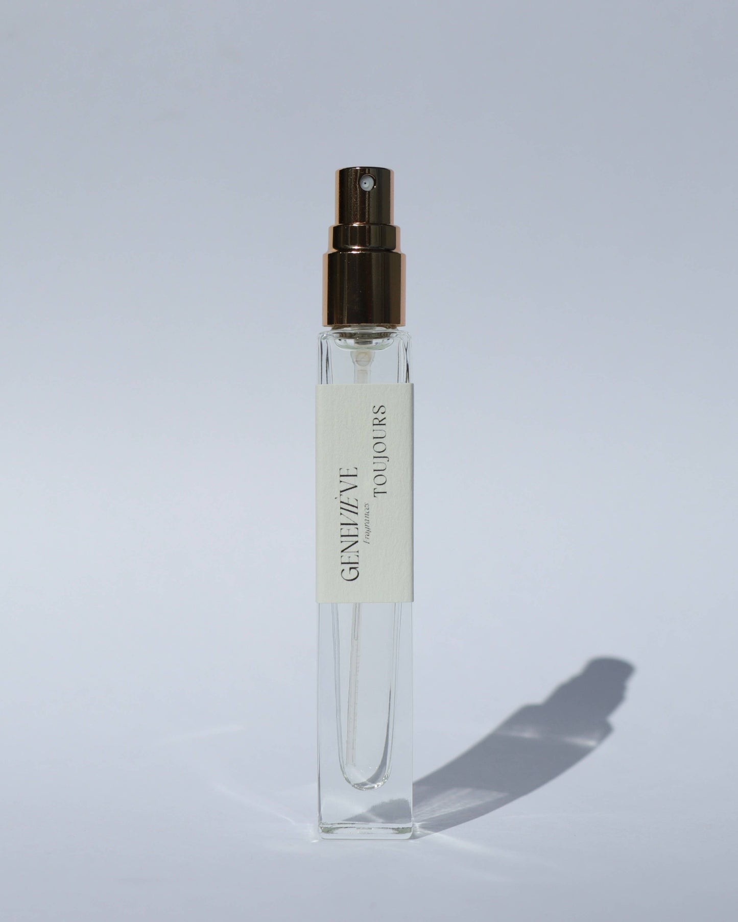 Small clear spray bottle with a gold cap on a light gray background