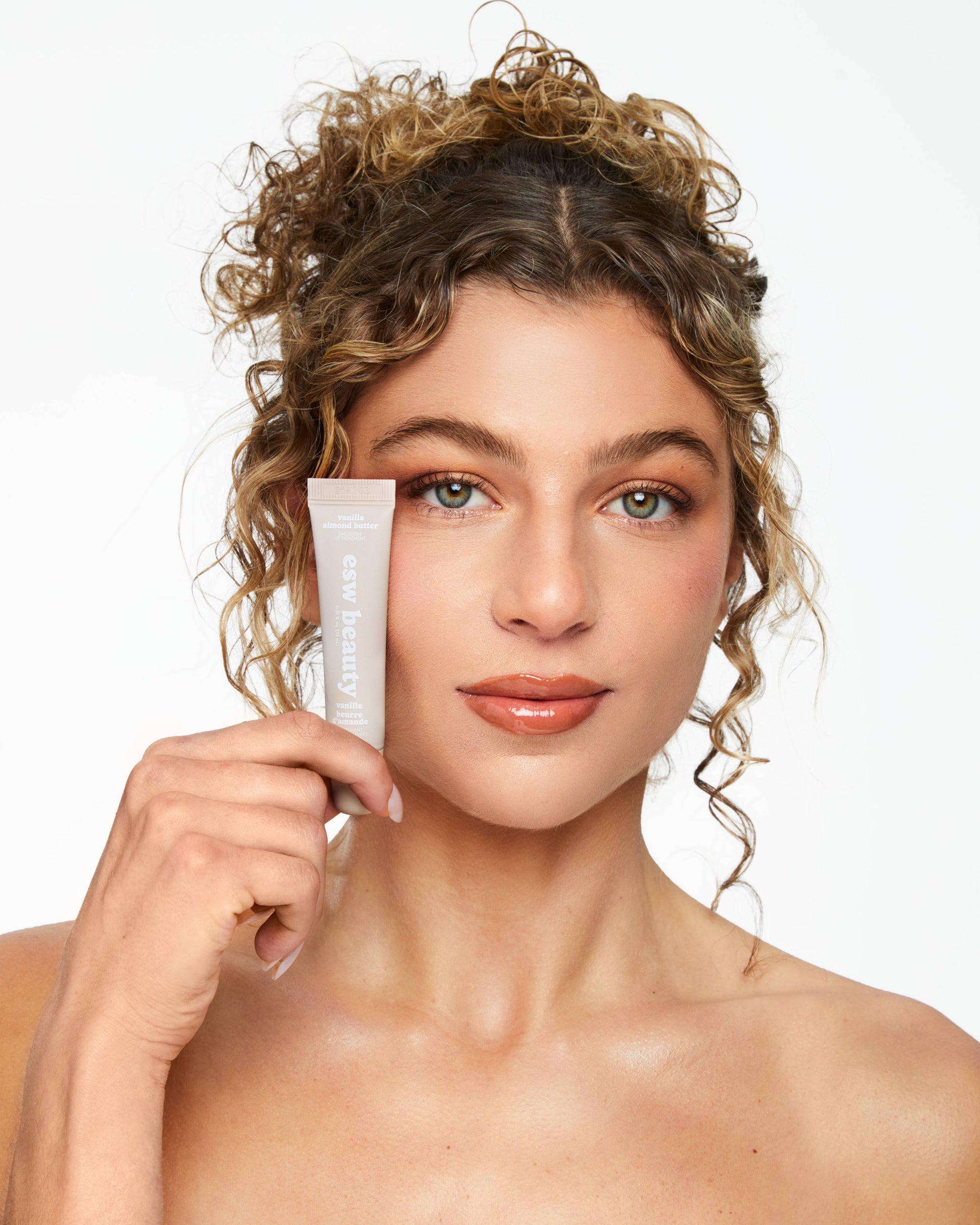 Woman holding a skincare product against a plain background