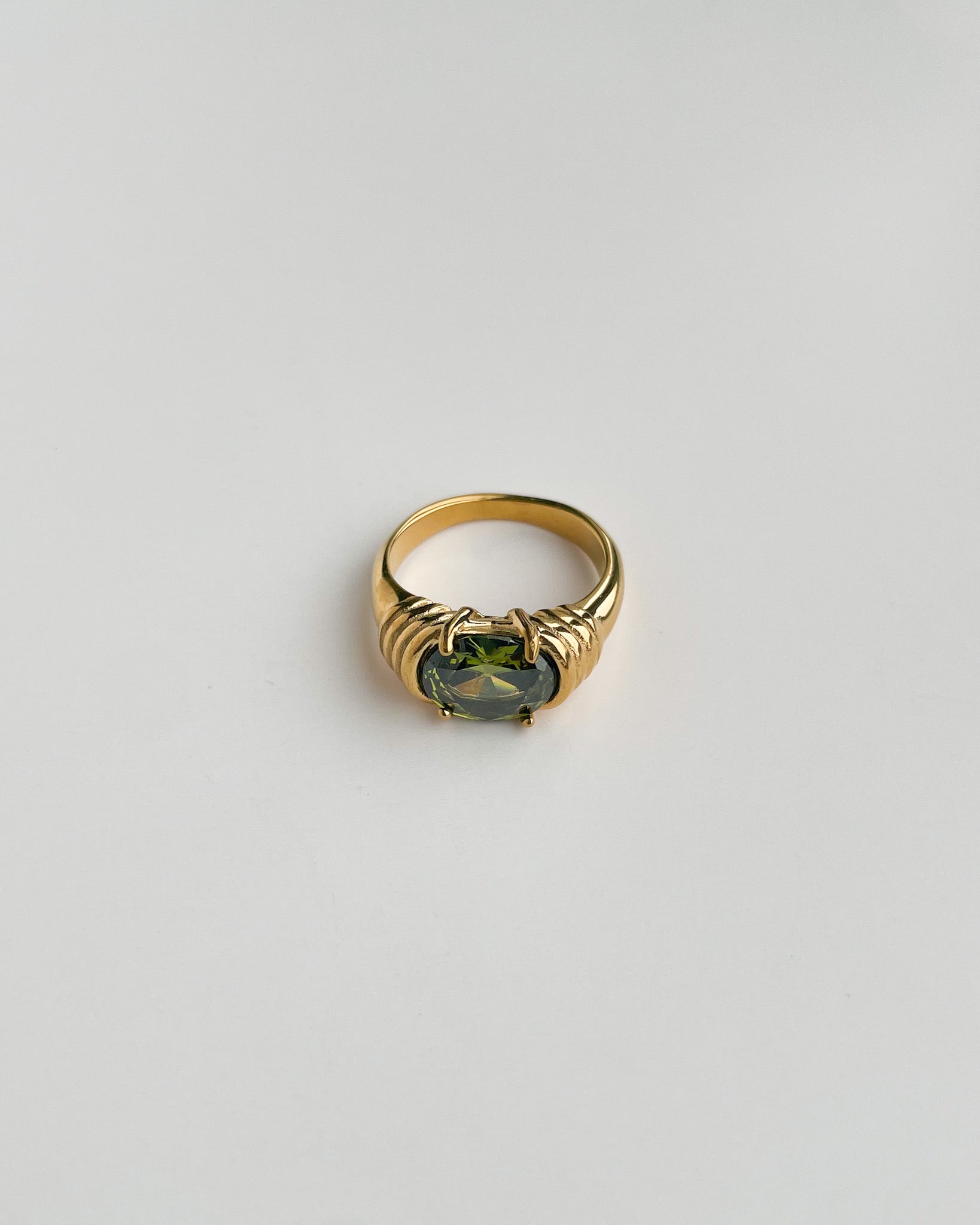 Gold ring with a green gemstone on a light gray background