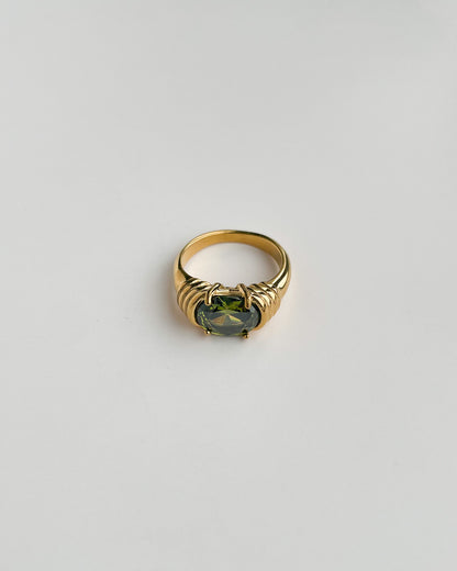 Gold ring with a green gemstone on a light gray background