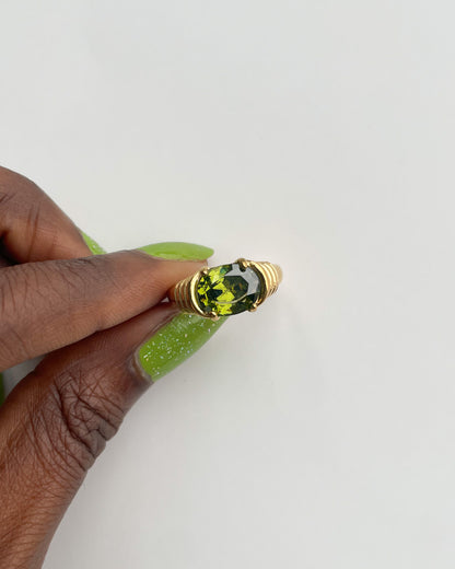 Gold ring with a green gemstone held by a hand on a white background