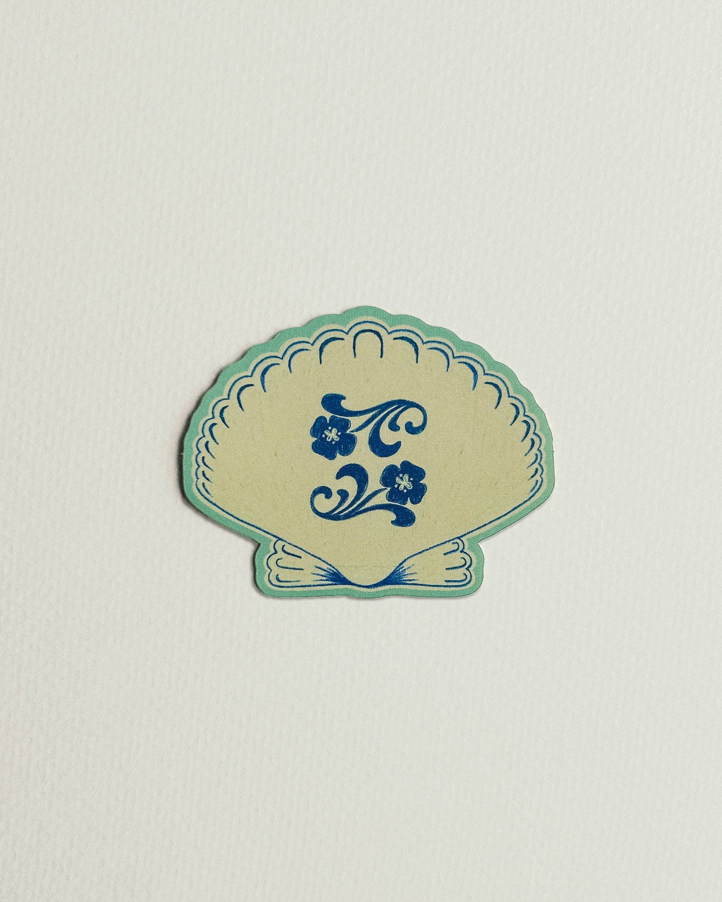Decorative shell-shaped sticker with blue floral design on a light gray background