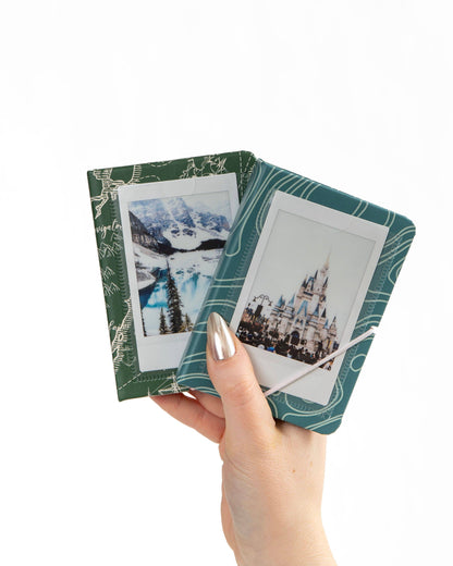 Two green photo albums with printed pictures held by a hand on a white background