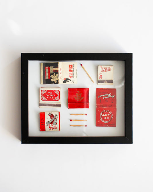 Framed display of matchboxes and matches on a white background