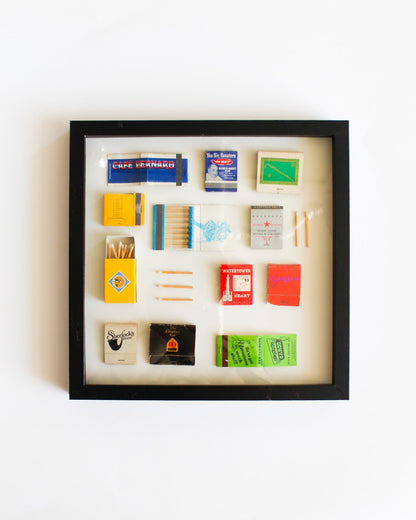 Framed display of matchbooks and matches on a white background