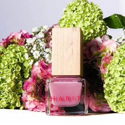 Pink nail polish bottle with wooden cap surrounded by green and pink flowers