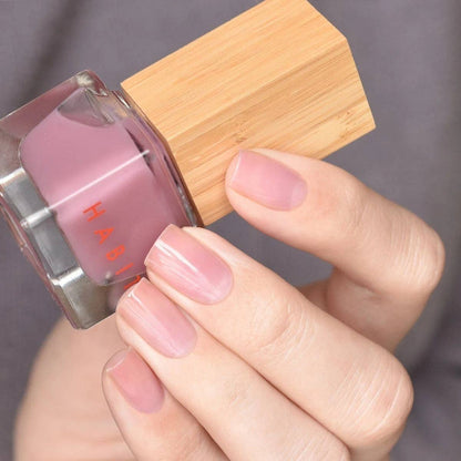 Hand holding a pink nail polish bottle with wooden applicator