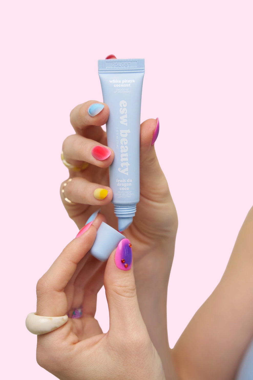 Hand holding a blue skincare product against a pink background