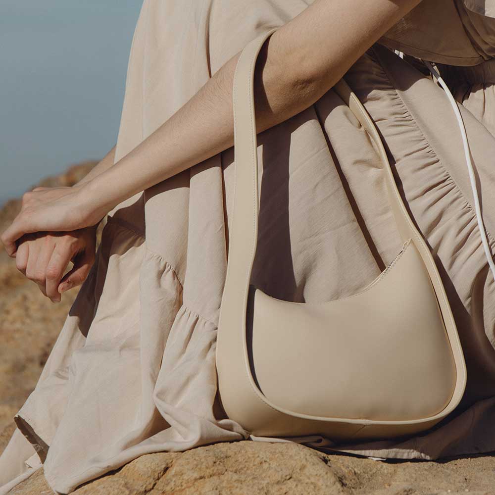 Person holding a beige handbag in a desert setting, Willow Shoulder Bag Melie Bianco
