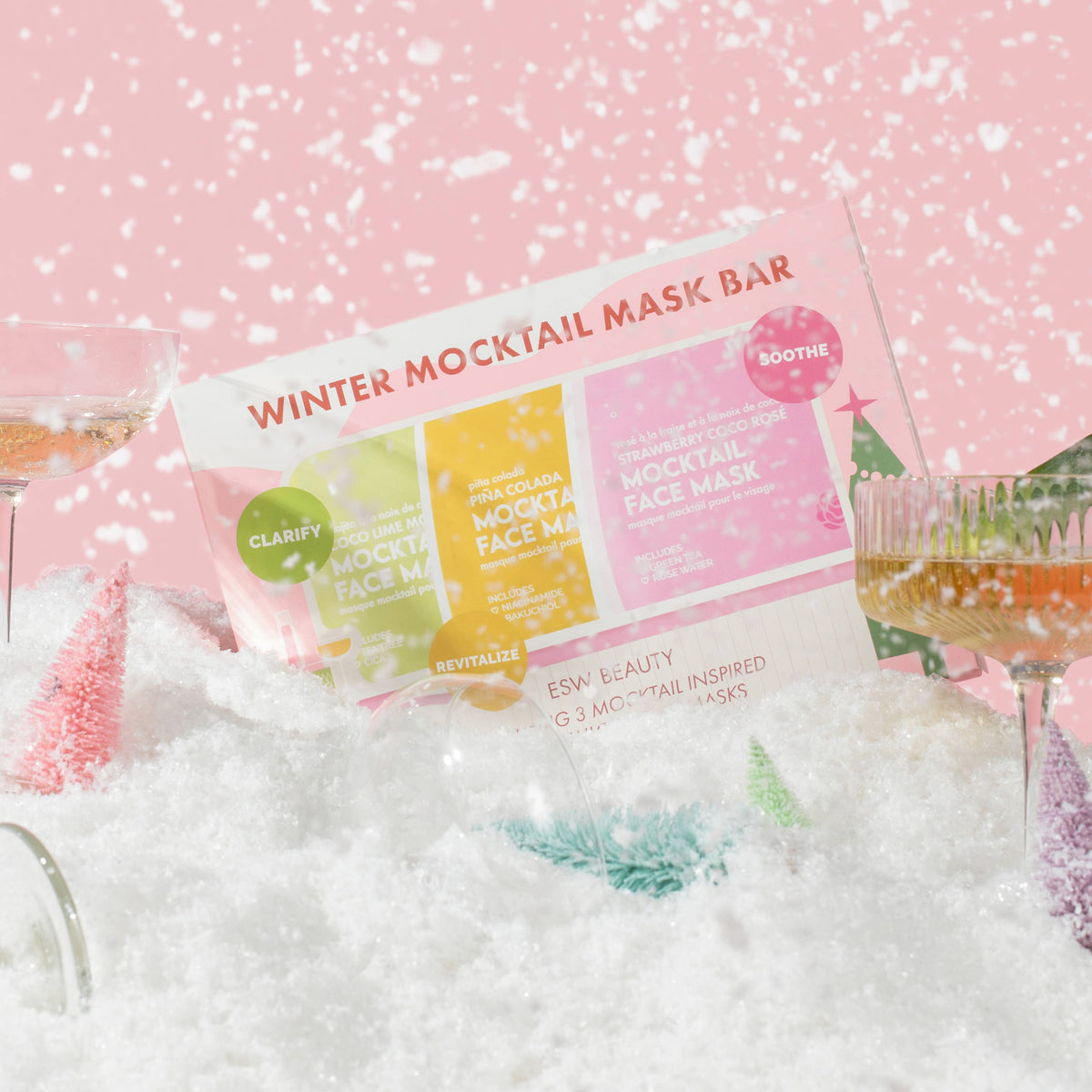 Winter Mocktail Mask Bar packaging displayed in a snowy styled setting with cocktail glasses and pink background.