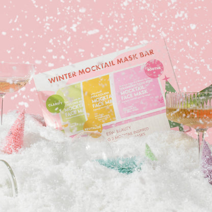 Winter Mocktail Mask Bar packaging displayed in a snowy styled setting with cocktail glasses and pink background.