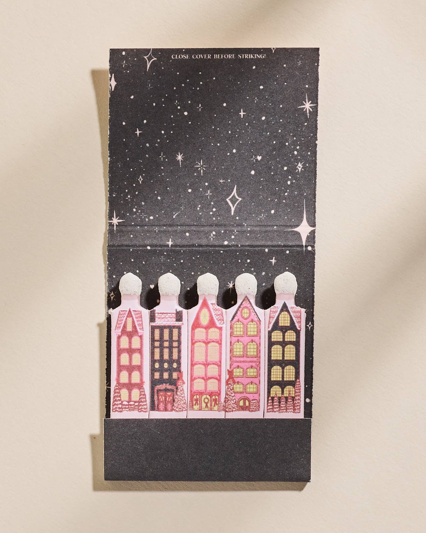 Notebook with illustrated houses and starry night design on a beige, background. Wintry Village Printed Matchbook