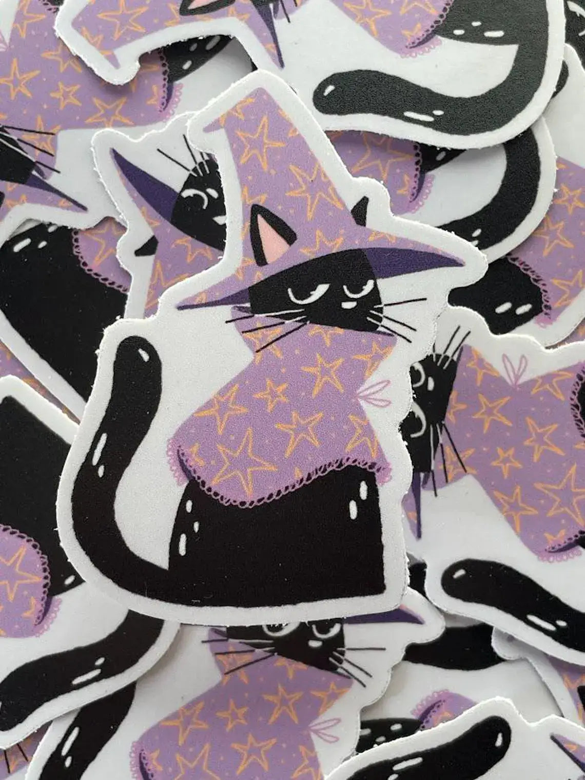 Stickers of black cats in witch hats on a purple background with stars.