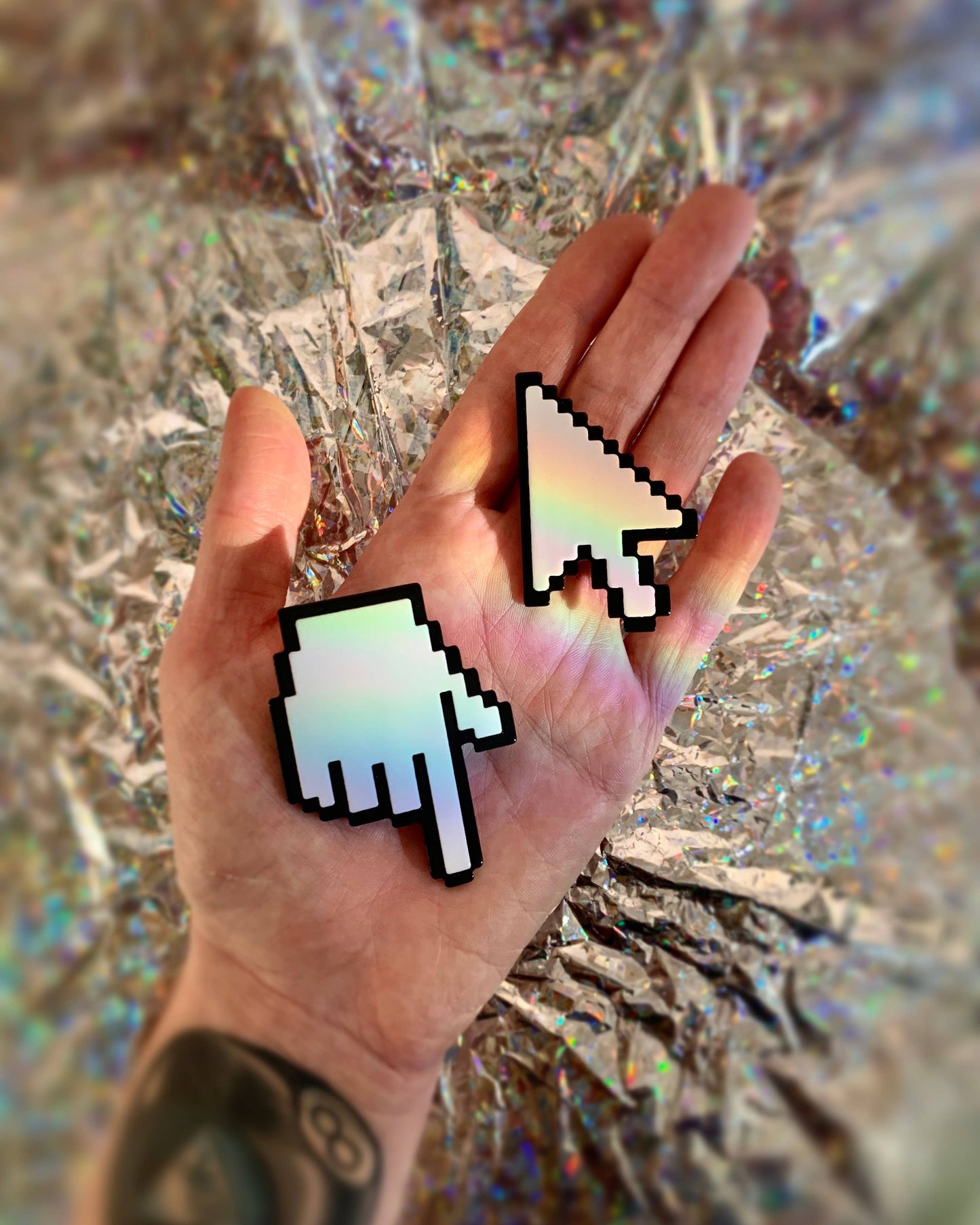 Hand wearing two pixelated cursor earrings against a reflective surface