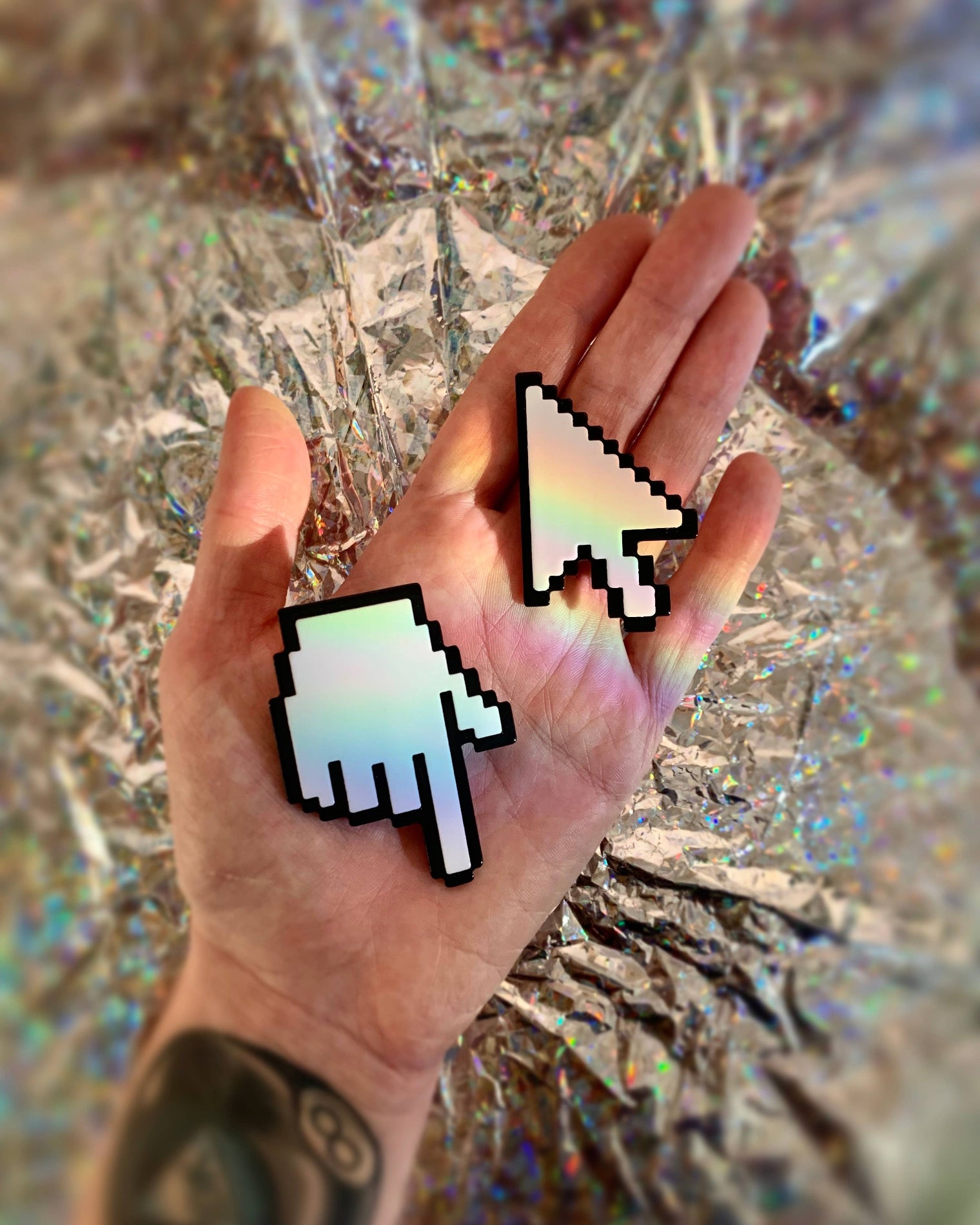 Hand wearing two pixelated cursor earrings against a reflective surface
