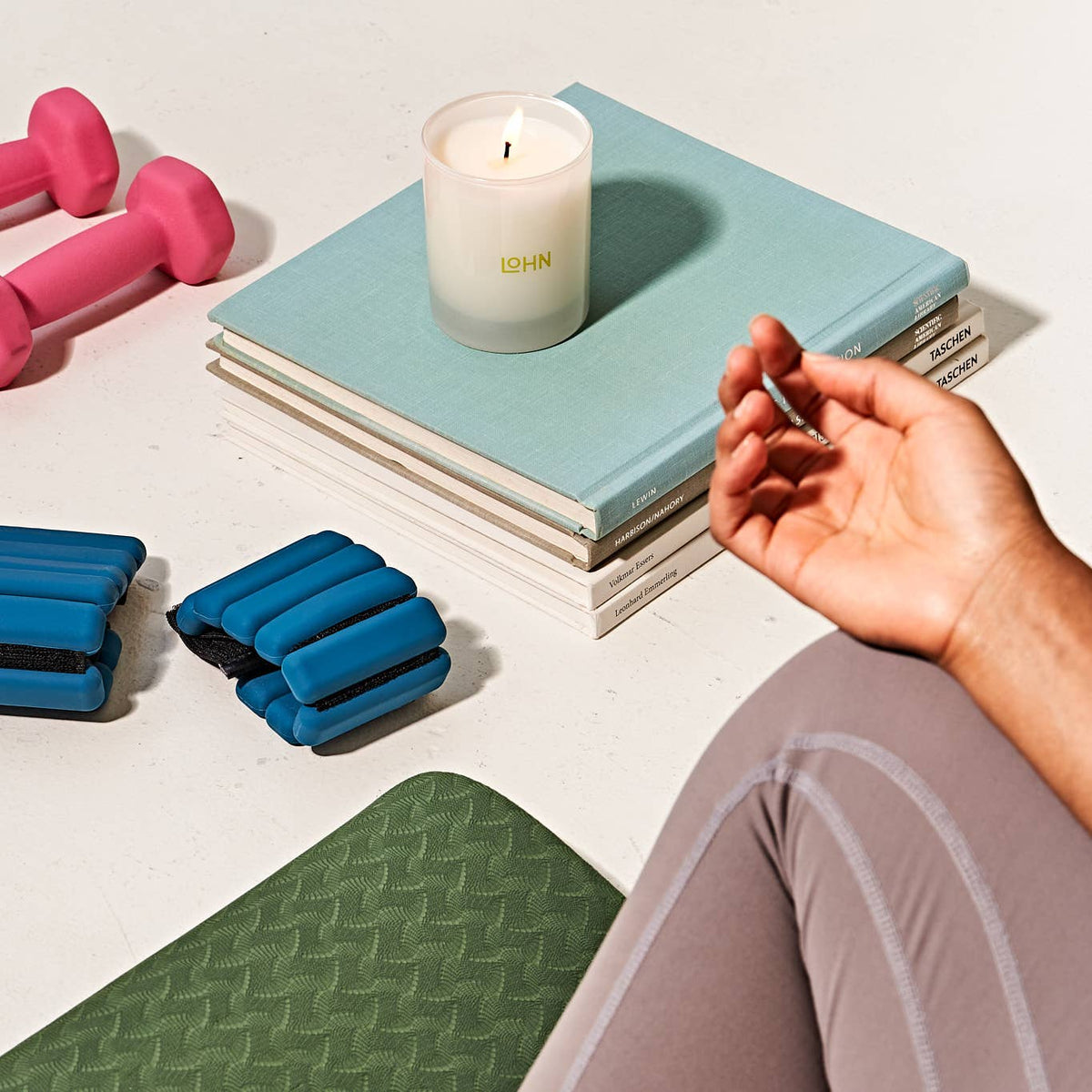 Hand lighting a candle on books with fitness equipment and a mat in the foreground