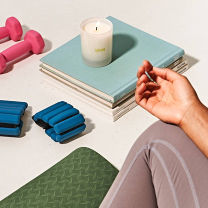 Hand lighting a candle on books with fitness equipment and a mat in the foreground