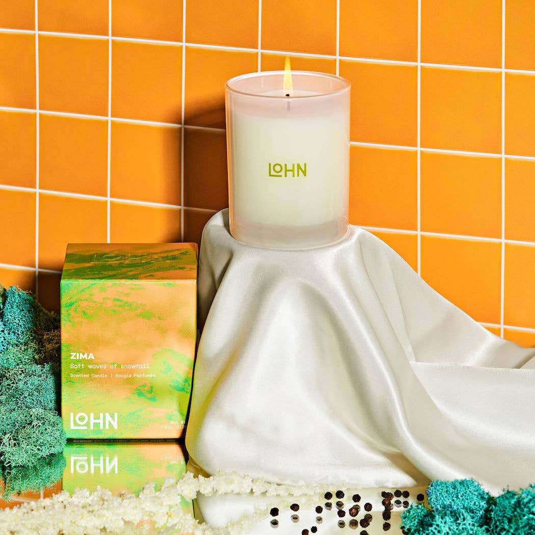 Candle with 'LOHN' branding on a white surface against an orange tiled wall.