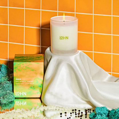 Candle with 'LOHN' branding on a white surface against an orange tiled wall.