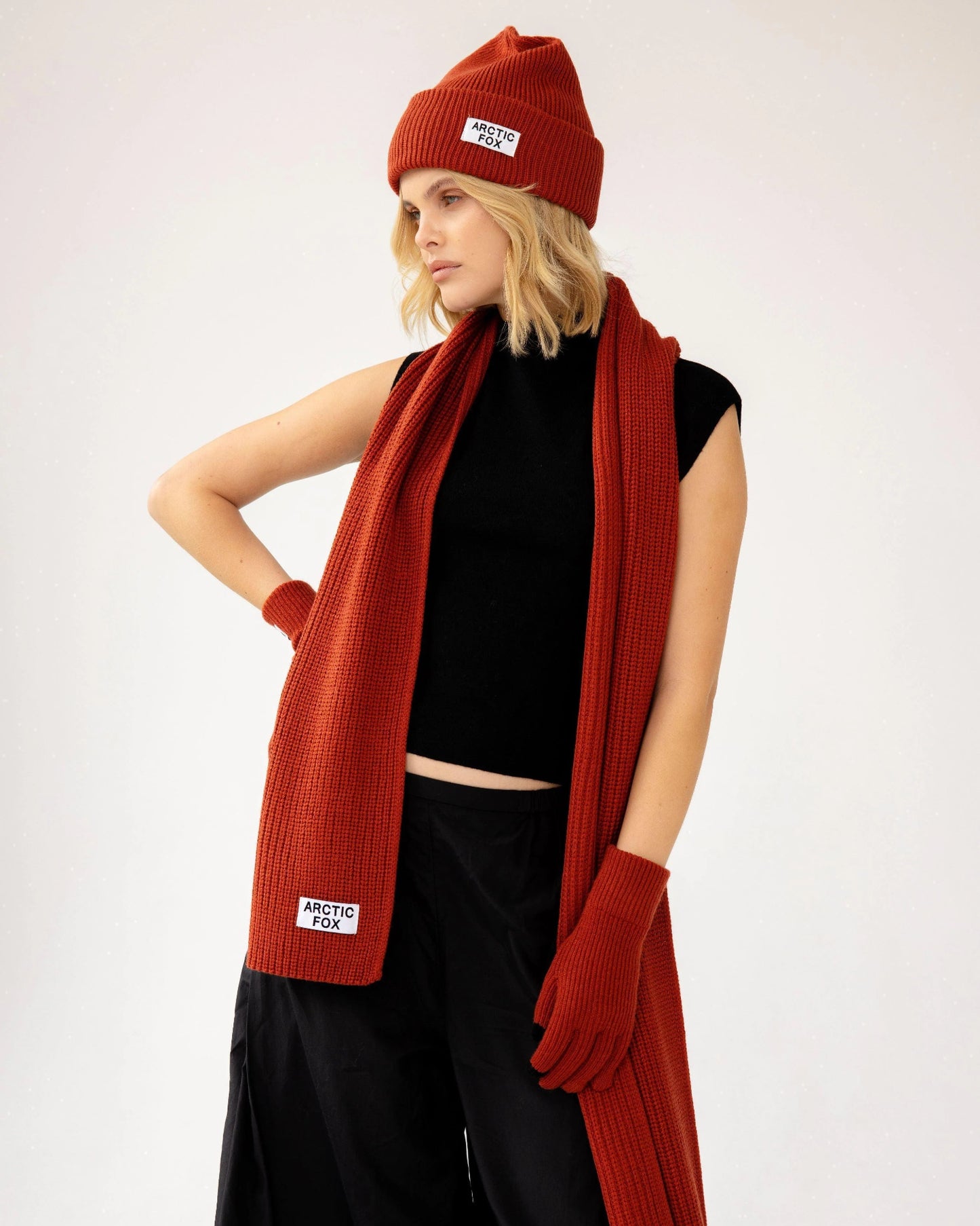 Person wearing a red scarf, beanie, and gloves on a white background, Terracotta Knitted Recycled Bottle Scarf