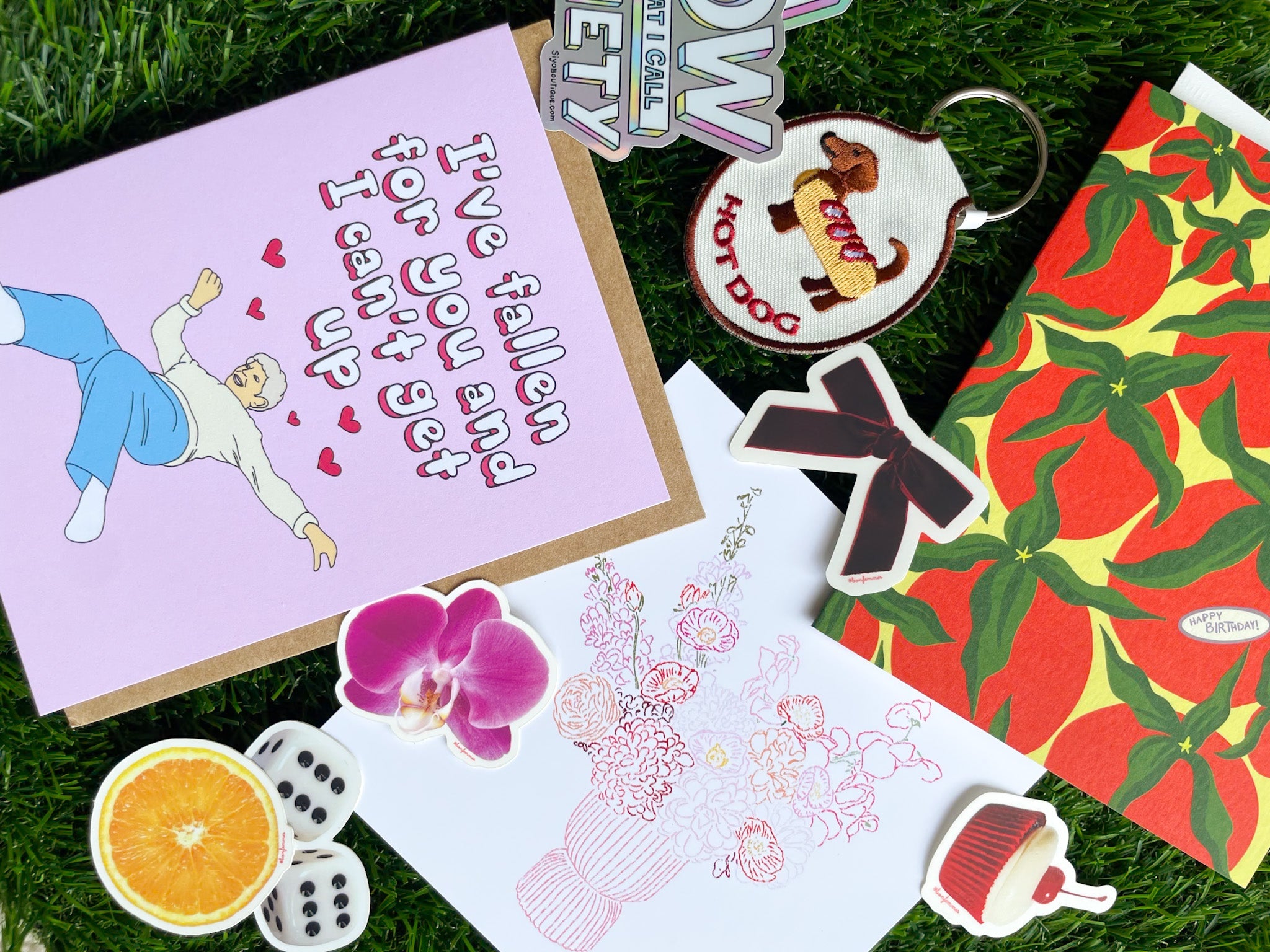 Collection of various items including a keychain, cards, and stickers on grass.