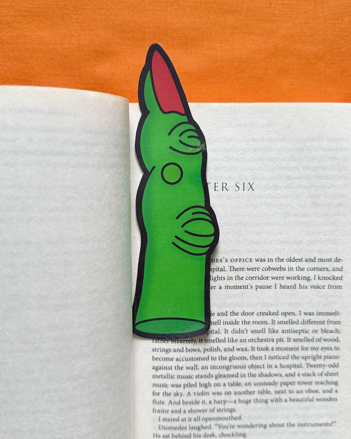 Green and red abstract art bookmark on an open book with an orange background