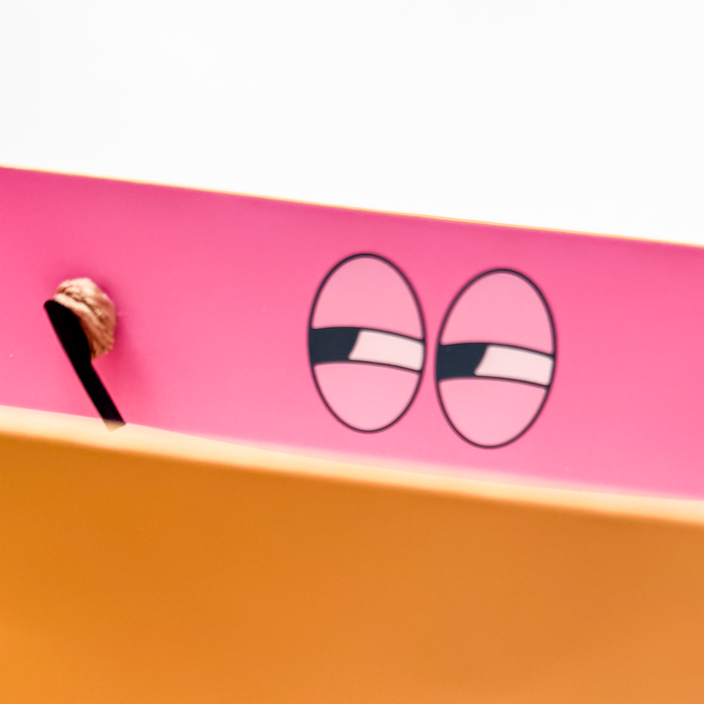 Close-up of a pink and orange gift bag with cartoonish eyes on the inside. no peeking gift bag
